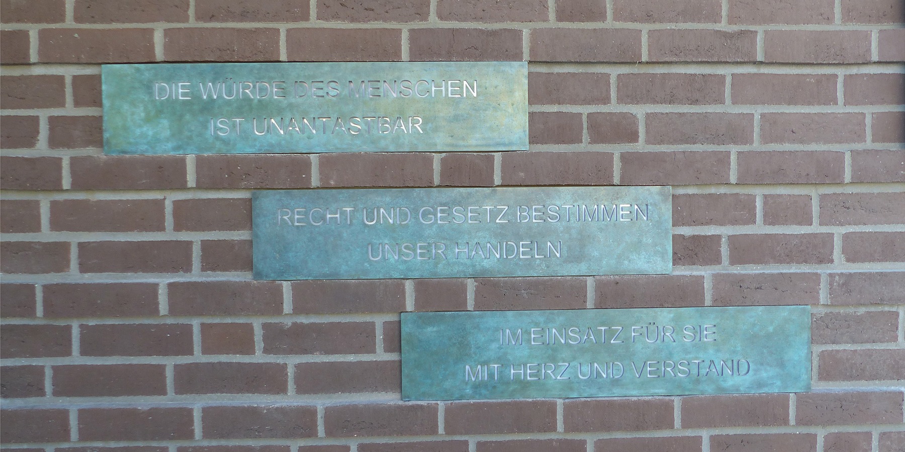 3 Bronzetafeln auf der Außenwand des Eingangsbereiches mit polizeilichen Grundsätzen als Teil der 4-teiligen Kunst am Bau-Installation des Künstlers Rainer Fest © 2023 SBL Greifswald