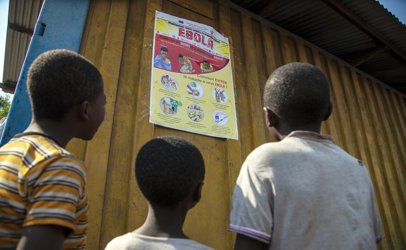 Drei Kinder blicken auf ein Plakat mit Hinweisen zur Vermeidung einer Ebolavirus-Infektion.