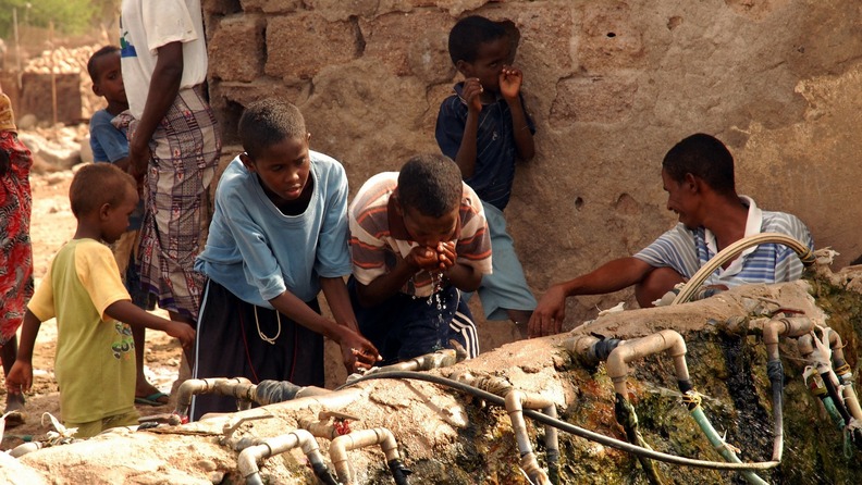 Kinder trinken Wasser von einem Brunnen.