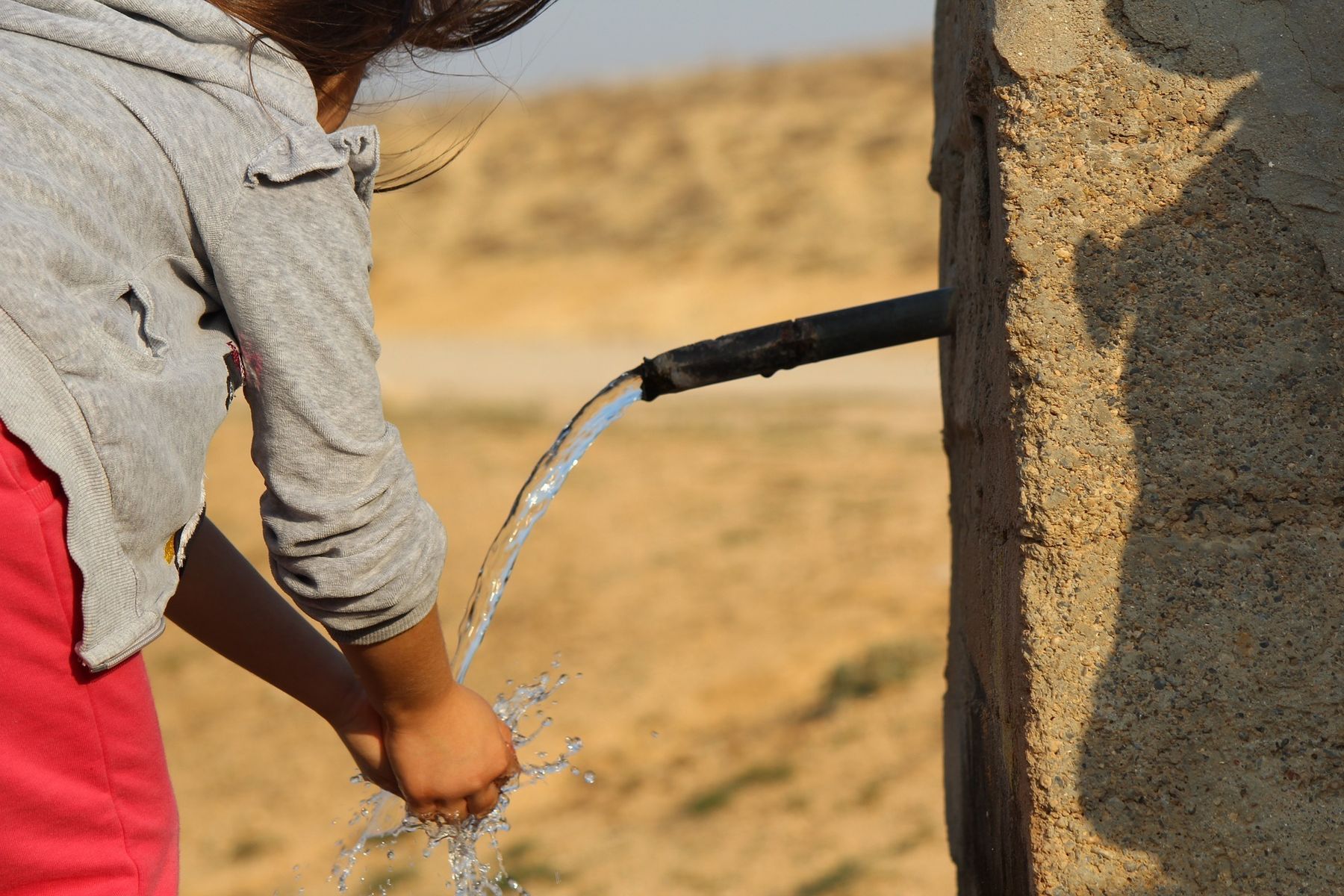 Mädchen wäscht sich bei Brunnen die Hände.