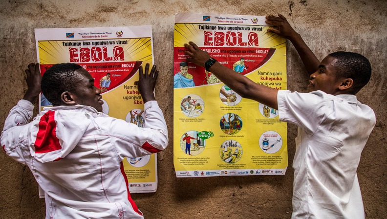 Zwei Helfer montieren Informationsplakate über die Prävention einer Ebola-Infektion. Zwei Helfer montieren Informationsplakate über die Prävention einer Ebola-Infektion.