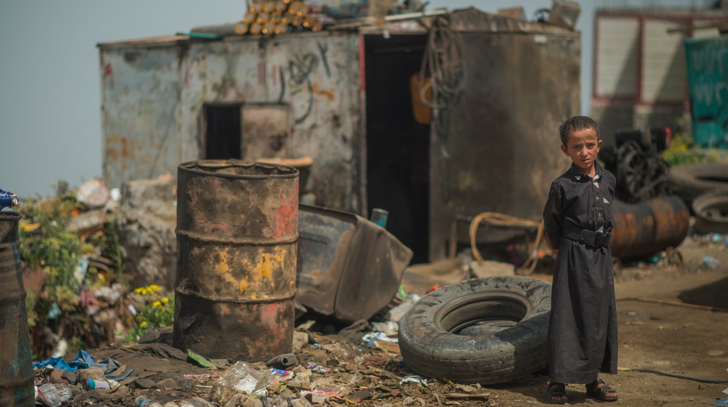 Jemen. Ein Kind steht, von Müll umgeben, vor einer Blechhütte.