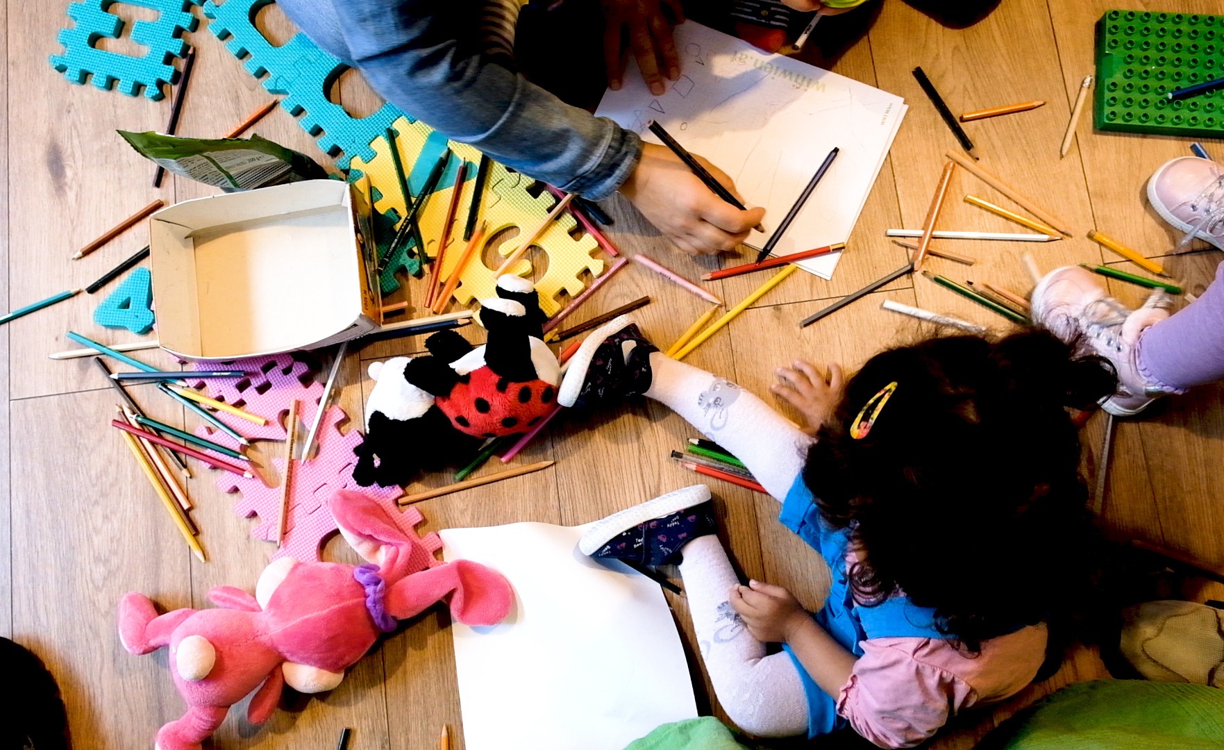 Ein Kind sitzt auf dem Boden, umgeben Zeichenpapier und Stiften.