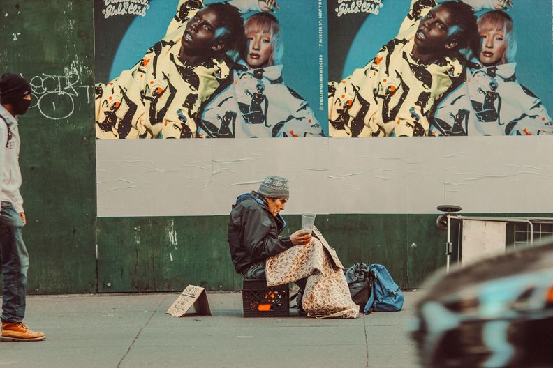 Obdachloser Mann sitzt mit Becher auf der Straße